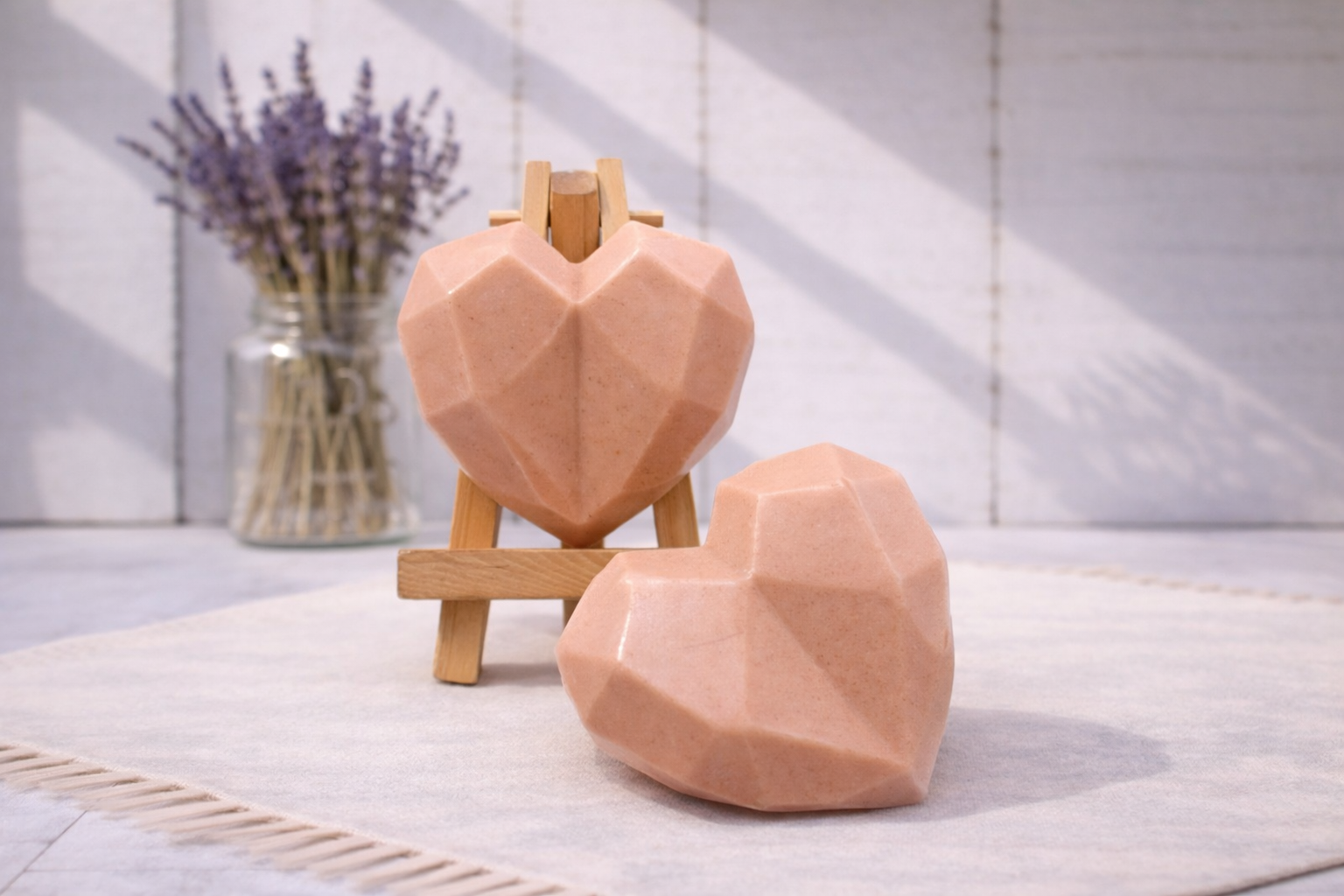 Two geometric heart-shaped vegan soaps on a stand with lavender in the background