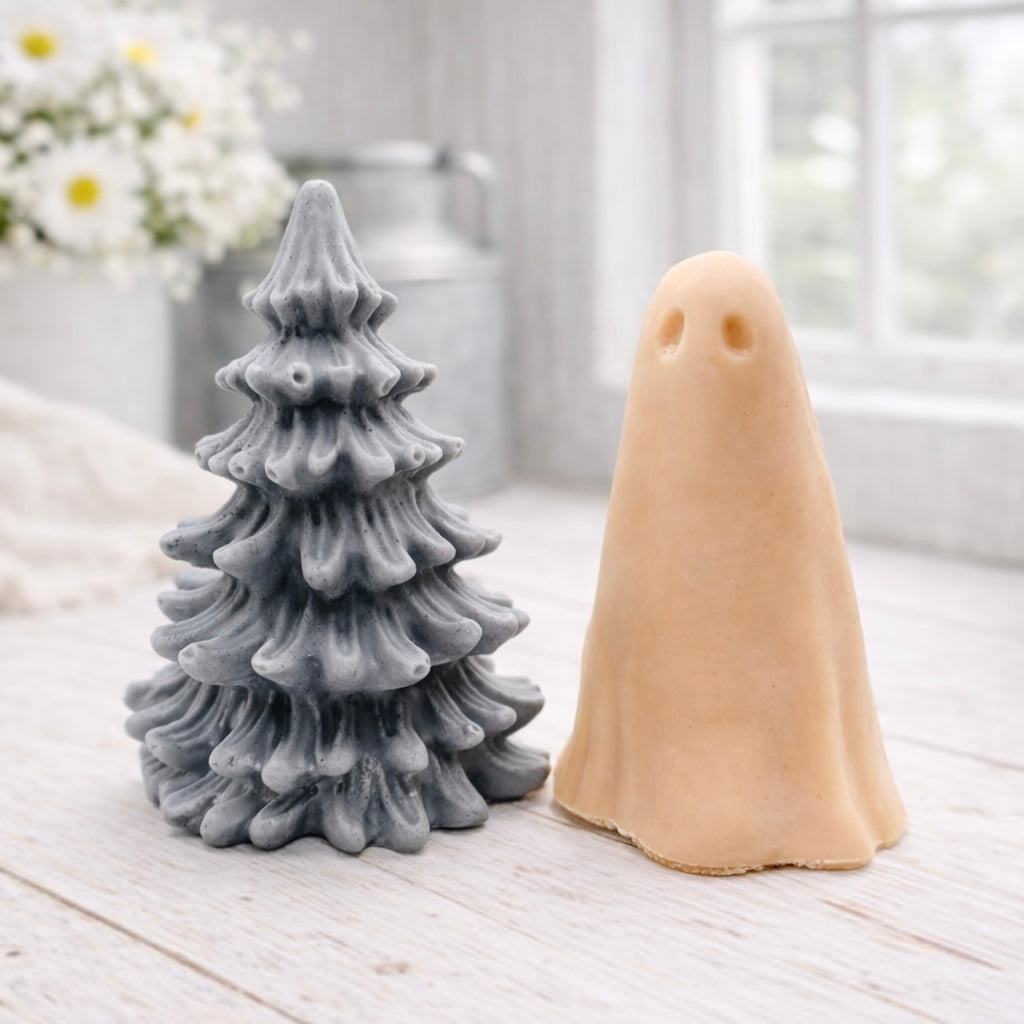 handmade ghost soap standing next to a grey textured Christmas tree sculpture soap, displayed on a rustic white wooden surface in a bright farmhouse decor setting.