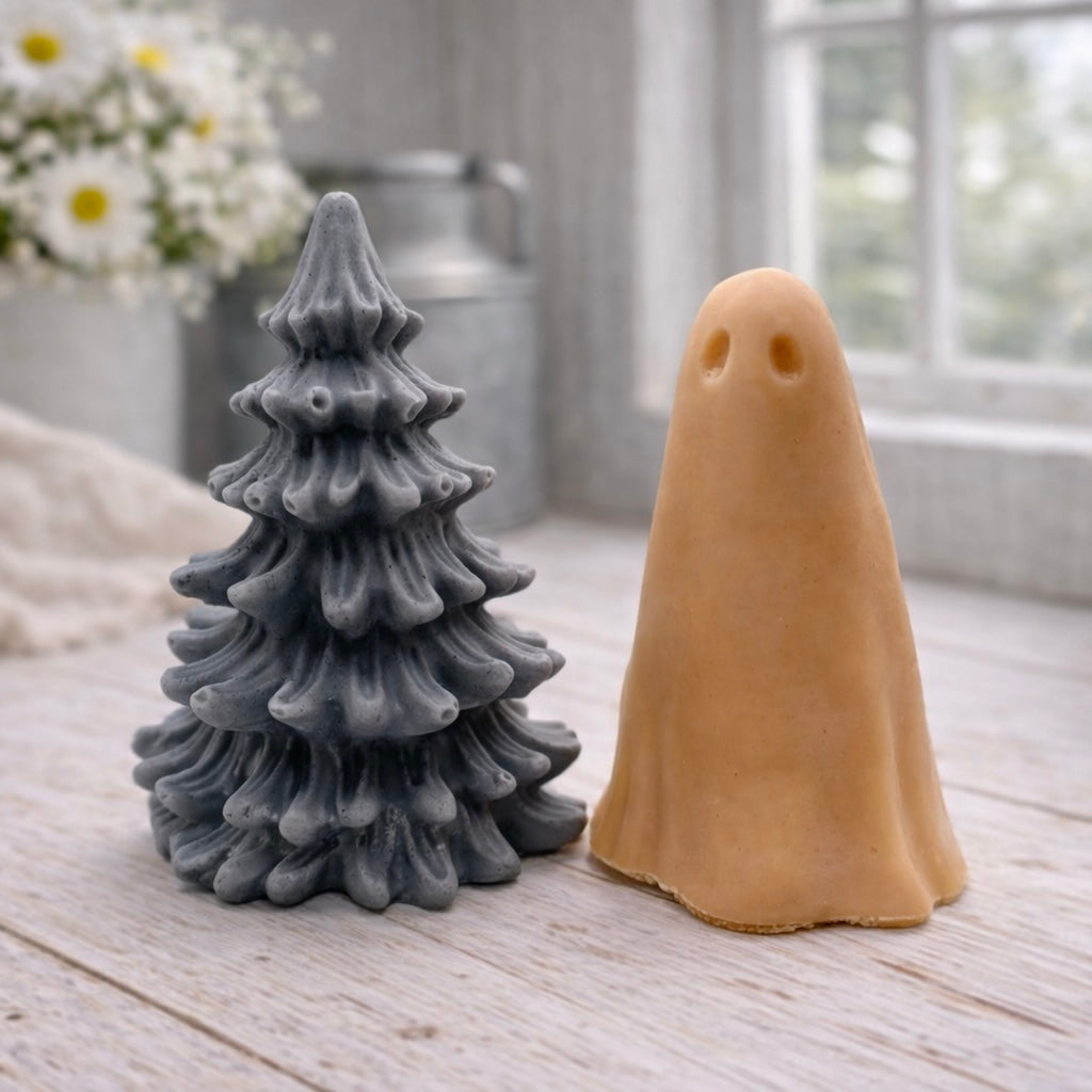 handmade ghost soap standing next to a grey textured Christmas tree sculpture soap, displayed on a rustic white wooden surface in a bright farmhouse decor setting.