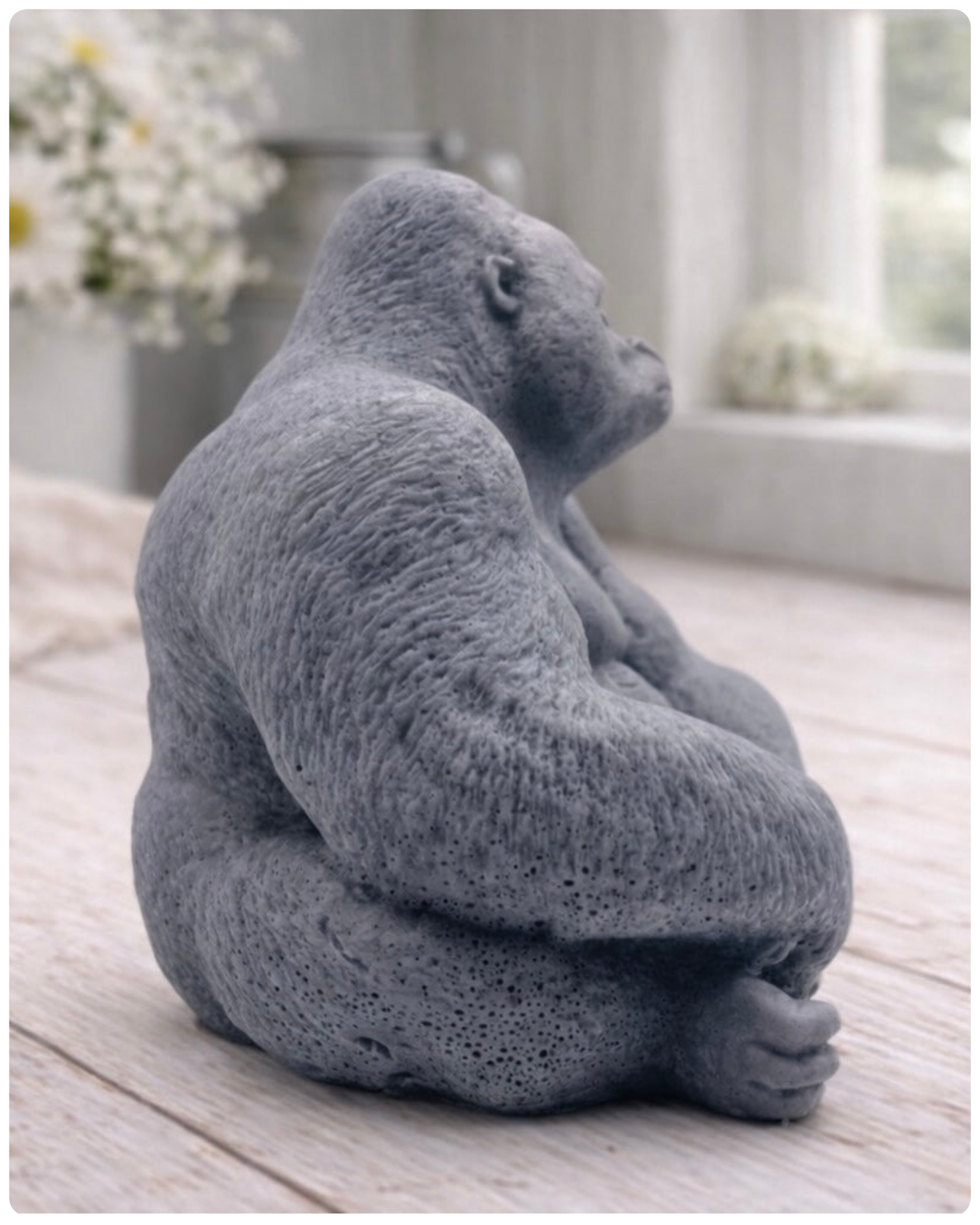 A highly detailed handmade vegan soap in a natural stone-grey colour, sculpted in the shape of a sitting gorilla with realistic fur and muscle textures, displayed on a light wooden surface.