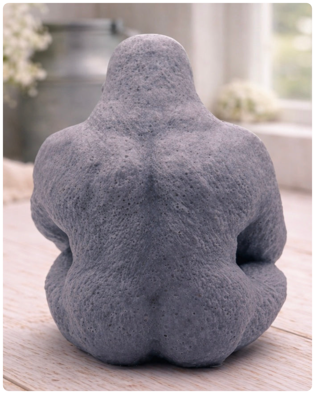 A highly detailed handmade vegan soap in a natural stone-grey colour, sculpted in the shape of a sitting gorilla with realistic fur and muscle textures, displayed on a light wooden surface.