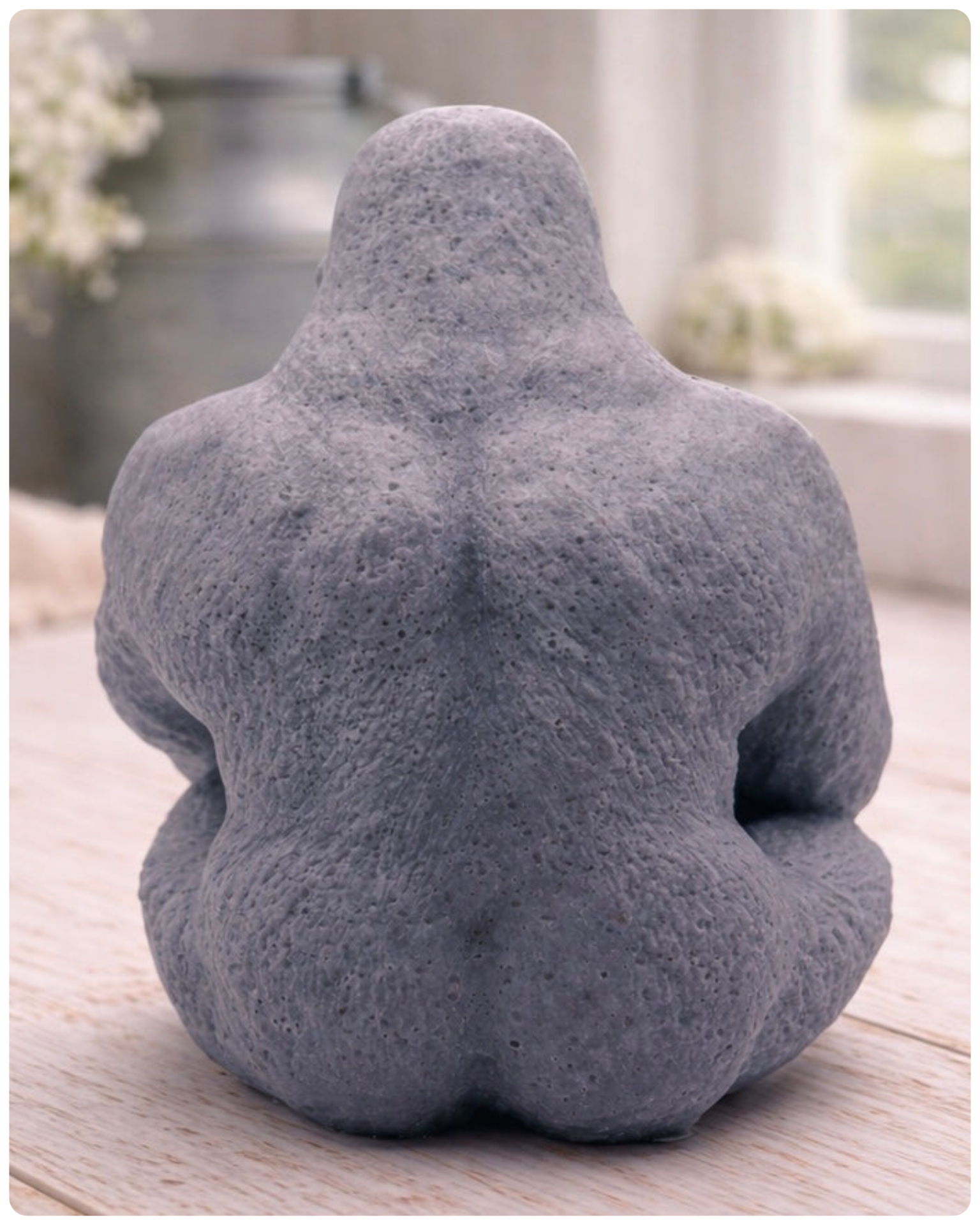 A highly detailed handmade vegan soap in a natural stone-grey colour, sculpted in the shape of a sitting gorilla with realistic fur and muscle textures, displayed on a light wooden surface.