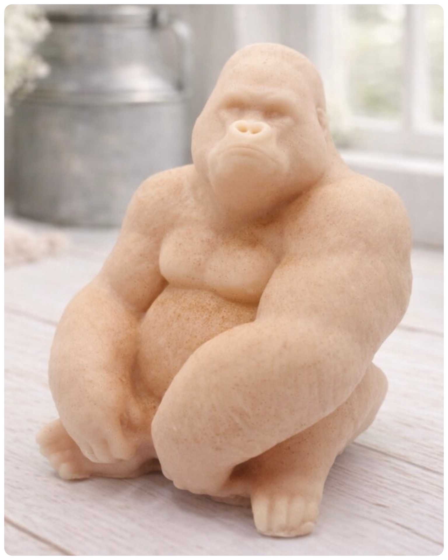 A highly detailed handmade vegan soap in a natural pink colour, sculpted in the shape of a sitting gorilla with realistic fur and muscle textures, displayed on a light wooden surface.