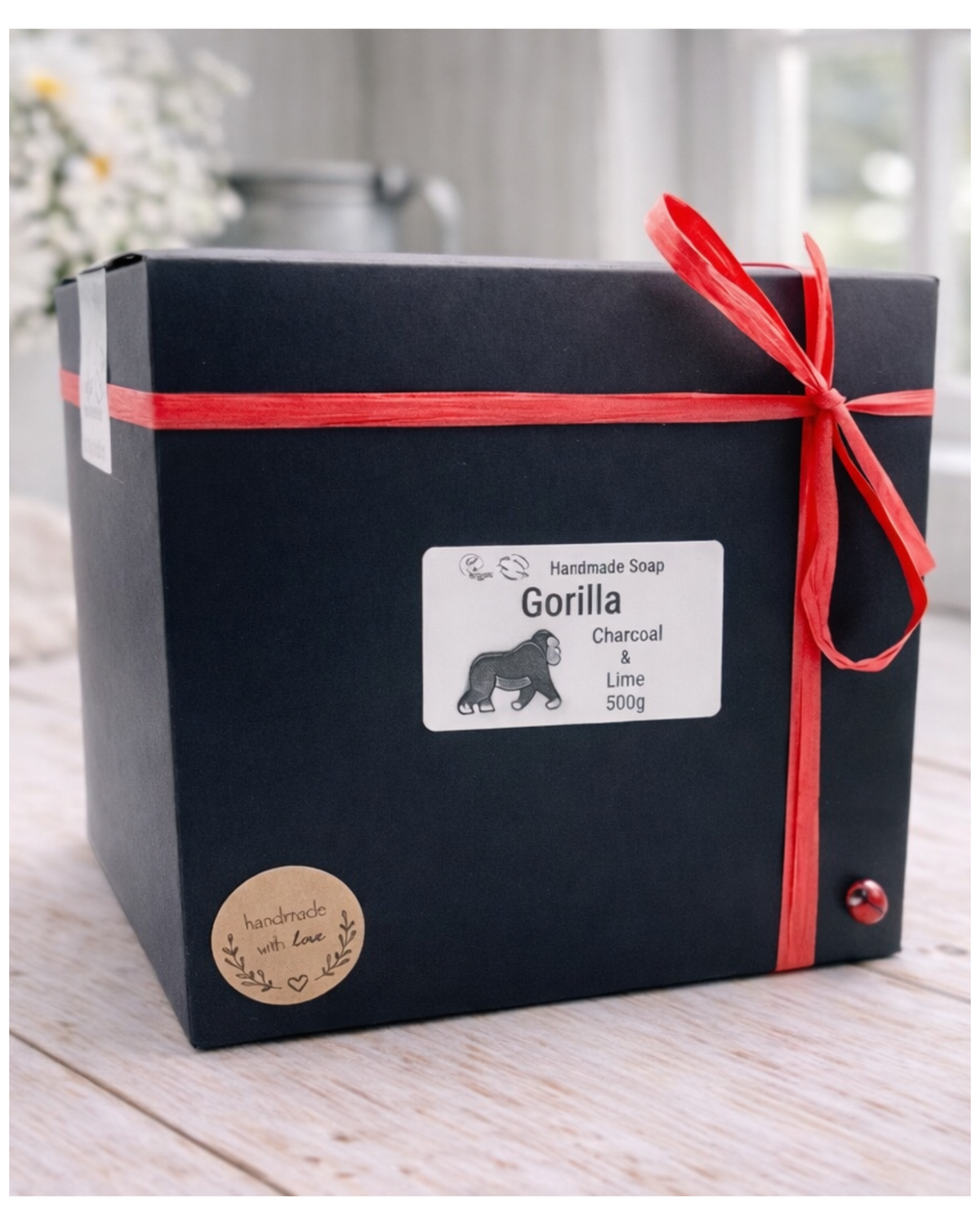 Black gift box with red ribbon and Gorilla Soap label on a wooden surface