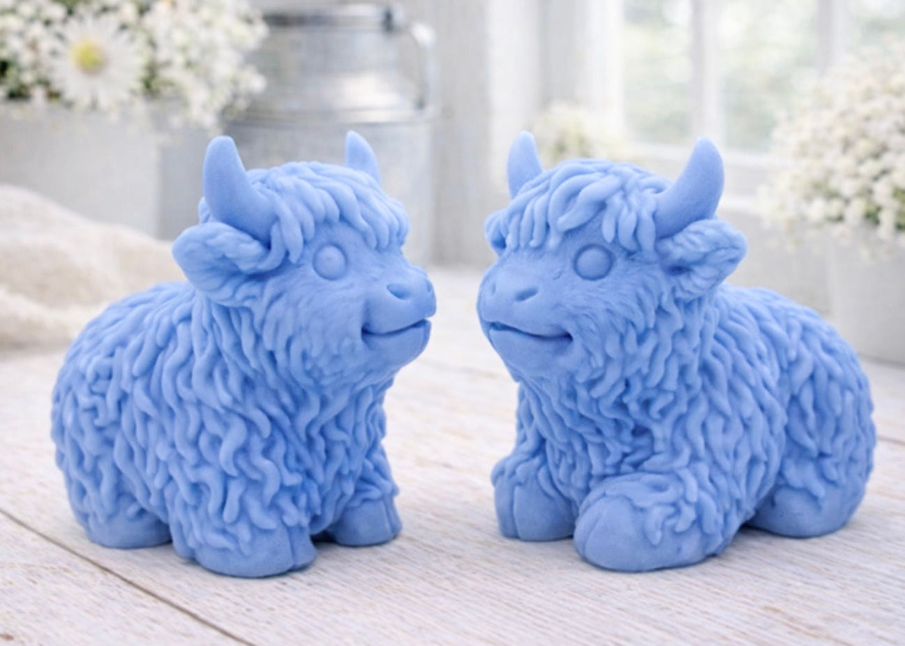 A highly detailed handmade vegan soap sculpted in the shape of a highland cow with long, flowing fur texture, a sweet face with a large snout, and prominent horns, displayed on a light wooden surface in a bright farmhouse setting.