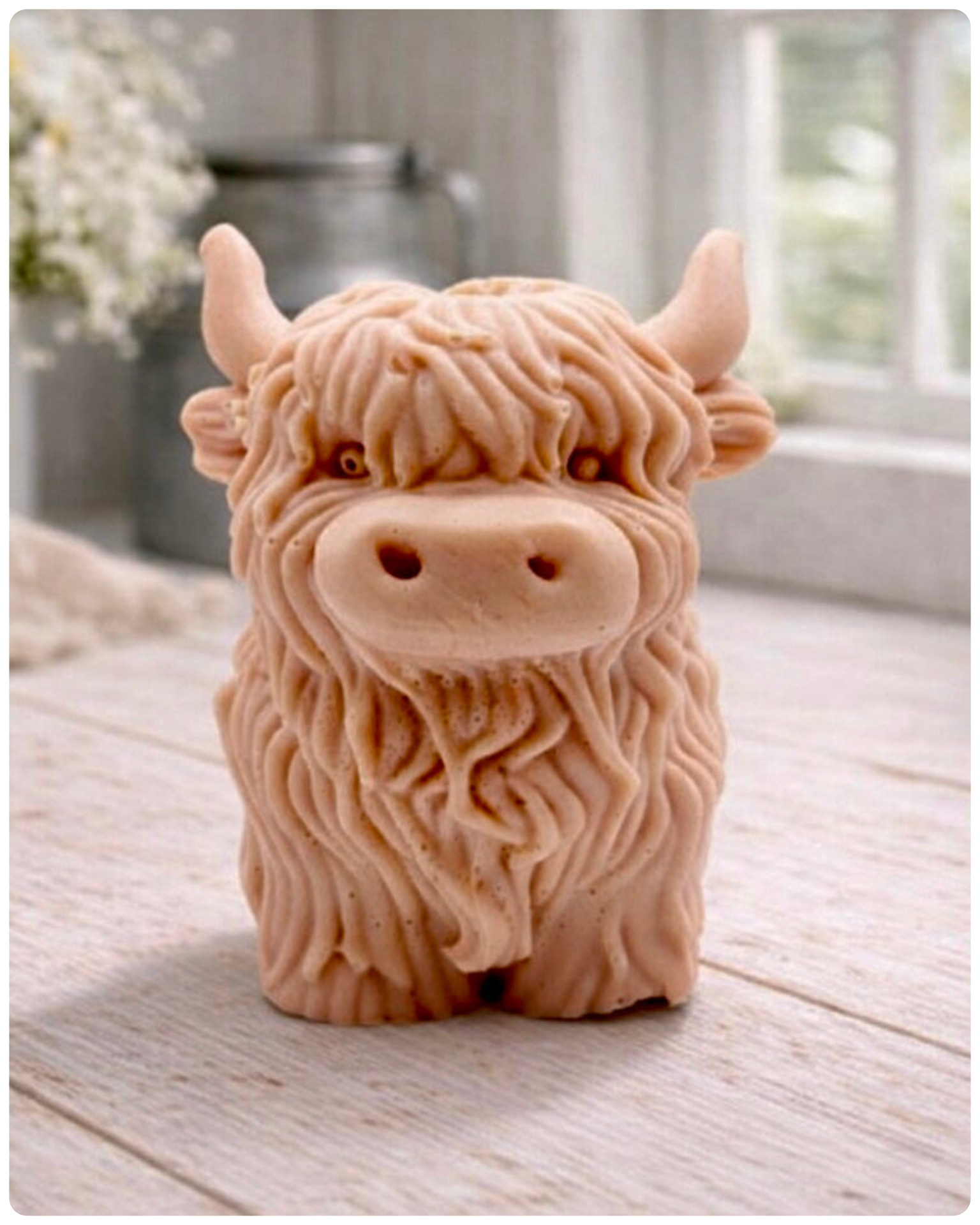 A detailed handmade vegan soap in a sculpted in the shape of a highland cow with characteristic long, wavy fur, horns, and a friendly face, displayed on a light wooden surface