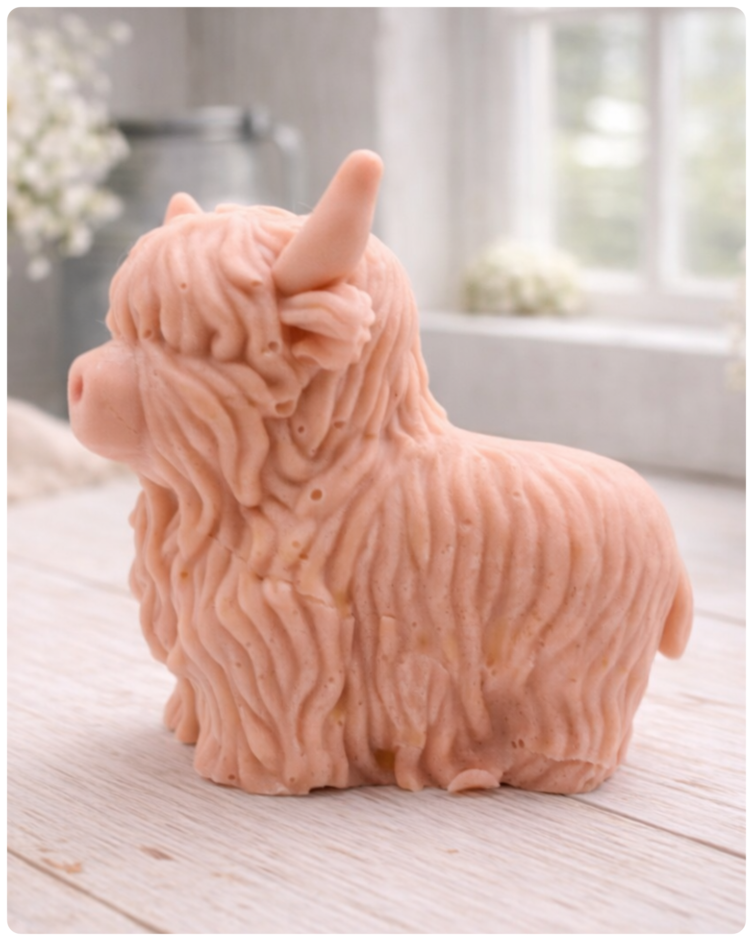 A detailed handmade vegan soap in a sculpted in the shape of a highland cow with characteristic long, wavy fur, horns, and a friendly face, displayed on a light wooden surface
