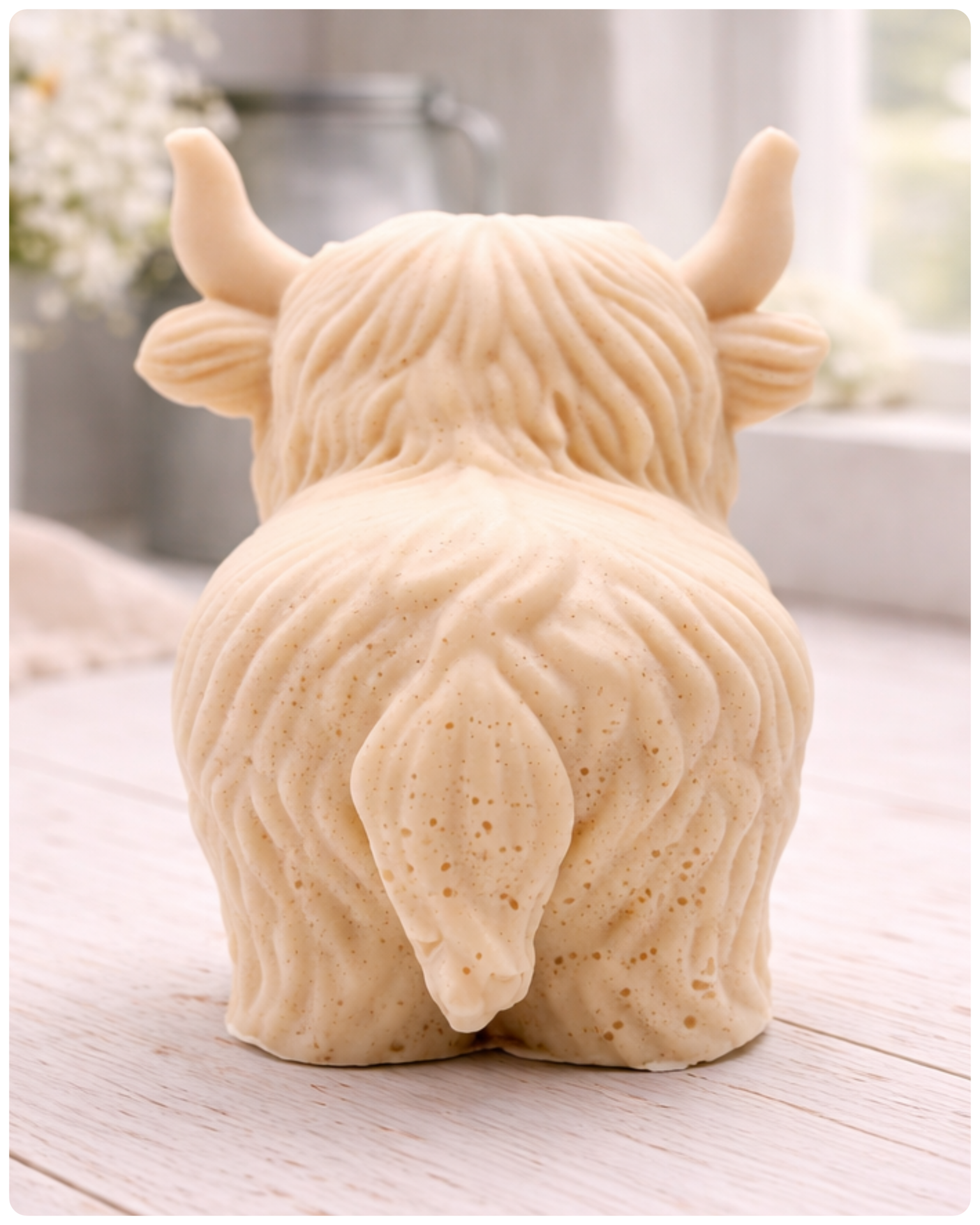 A detailed handmade vegan soap in a sculpted in the shape of a highland cow with characteristic long, wavy fur, horns, and a friendly face, displayed on a light wooden surface