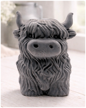 Load image into Gallery viewer, A detailed handmade vegan soap in a sculpted in the shape of a highland cow with characteristic long, wavy fur, horns, and a friendly face, displayed on a light wooden surface
