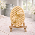 handmade vegan soap featuring an oval relief sculpture of two honey bees crawling on a honeycomb pattern, displayed on a small wooden easel in a bright farmhouse decor setting.