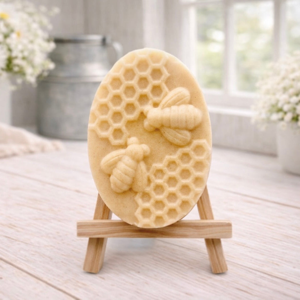 handmade vegan soap featuring an oval relief sculpture of two honey bees crawling on a honeycomb pattern, displayed on a small wooden easel in a bright farmhouse decor setting.
