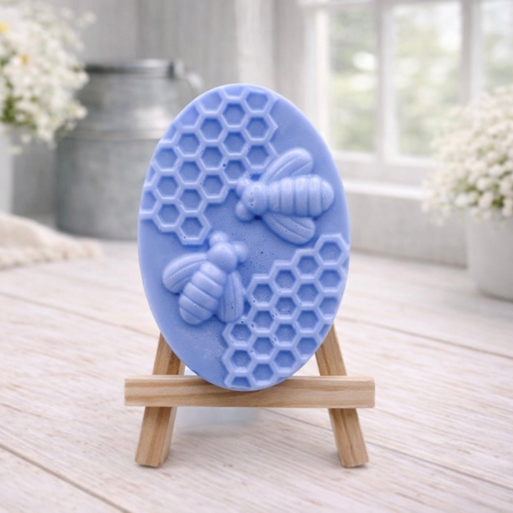 handmade vegan soap featuring an oval relief sculpture of two honey bees crawling on a honeycomb pattern, displayed on a small wooden easel in a bright farmhouse decor setting.