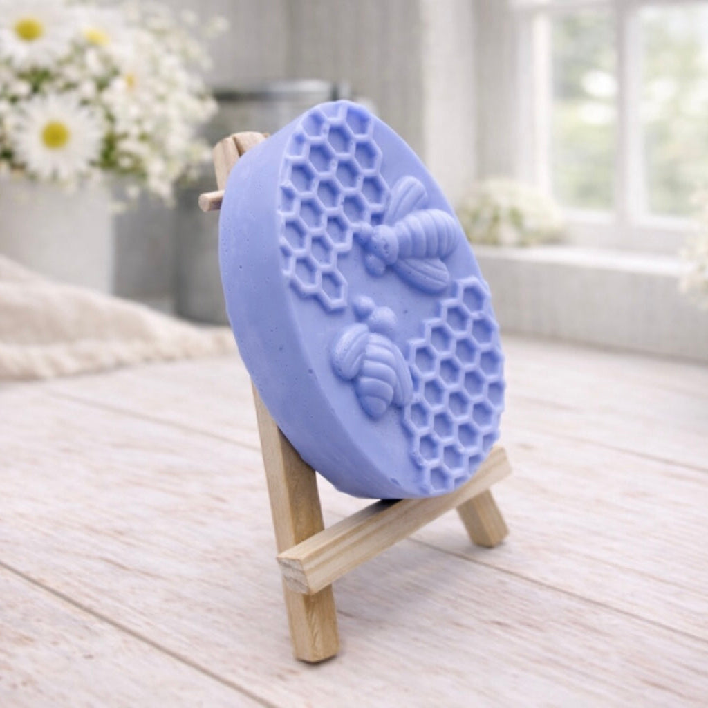 handmade vegan soap featuring an oval relief sculpture of two honey bees crawling on a honeycomb pattern, displayed on a small wooden easel in a bright farmhouse decor setting.