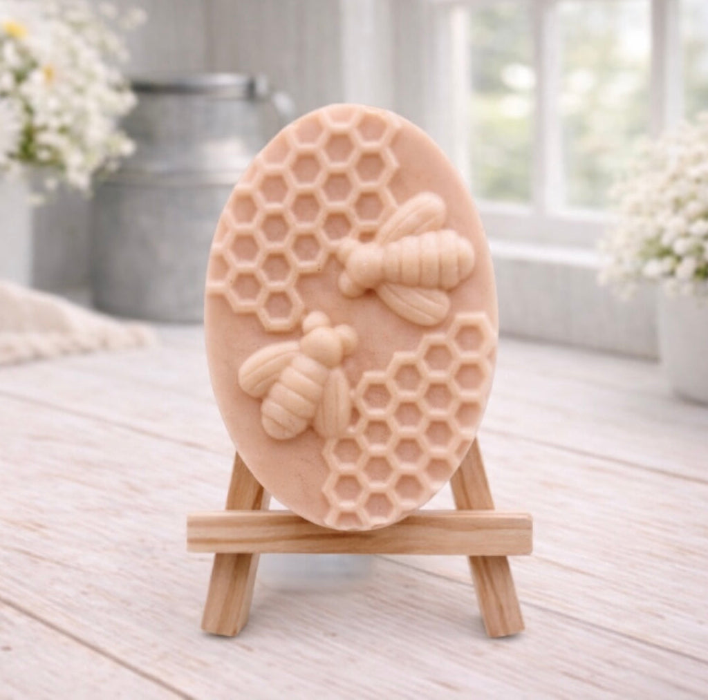 handmade vegan soap featuring an oval relief sculpture of two honey bees crawling on a honeycomb pattern, displayed on a small wooden easel in a bright farmhouse decor setting.