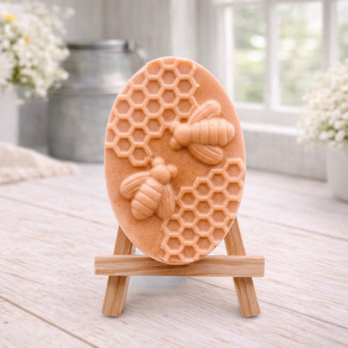 handmade vegan soap featuring an oval relief sculpture of two honey bees crawling on a honeycomb pattern, displayed on a small wooden easel in a bright farmhouse decor setting.