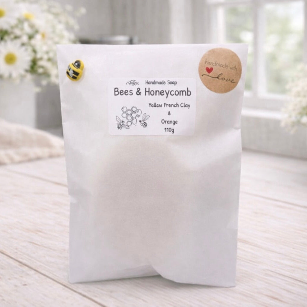 White soap packaging with a label on a light wooden surface, surrounded by flowers.