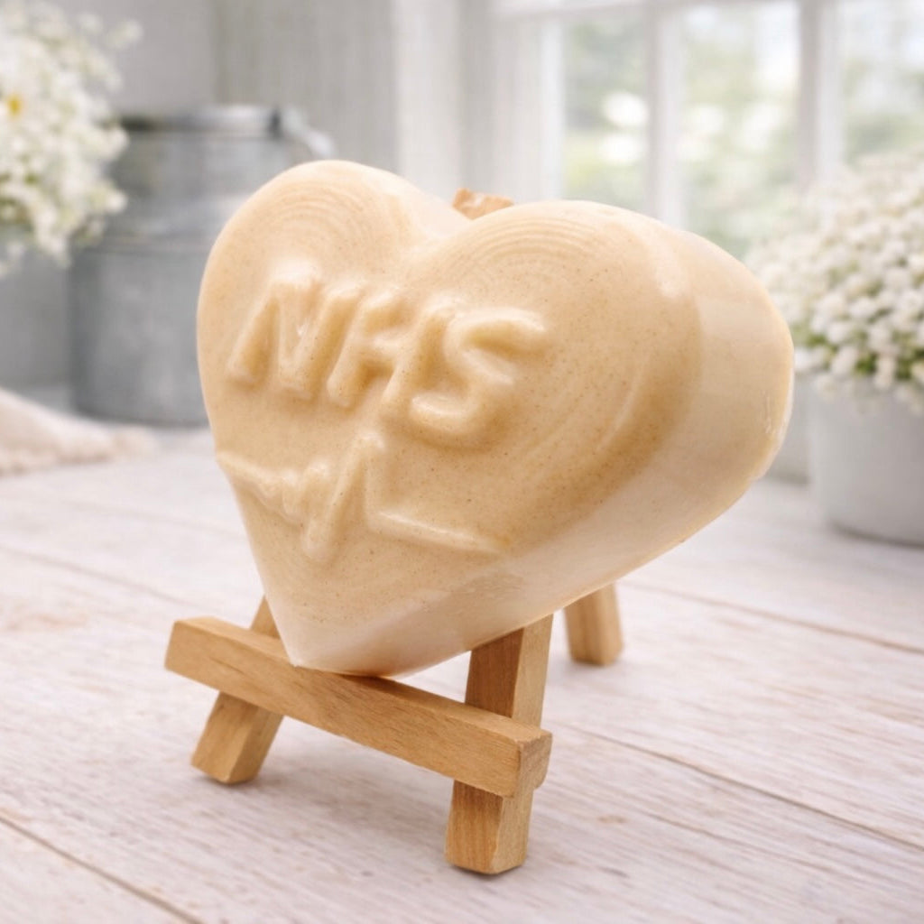 handmade vegan soap in a heart shape featuring an "NHS" relief and a heartbeat pulse line, displayed on a small wooden easel in a bright farmhouse decor setting.