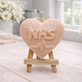 handmade vegan soap in a heart shape featuring an "NHS" relief and a heartbeat pulse line, displayed on a small wooden easel in a bright farmhouse decor setting.