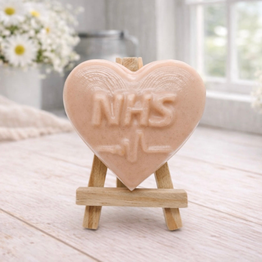 handmade vegan soap in a heart shape featuring an "NHS" relief and a heartbeat pulse line, displayed on a small wooden easel in a bright farmhouse decor setting.