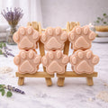 Six handmade vegan soaps in the shape of animal paw prints, displayed on two wooden easels in a spa-like setting with lavender and bath salts. Gift boxed. 