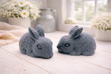 Load image into Gallery viewer, Set of two handmade vegan soaps in the shape of realistic crouching rabbits with detailed fur texture, displayed on a rustic white wooden surface in a bright farmhouse decor setting. Gift boxed. 

