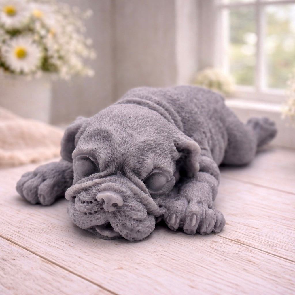 A highly detailed handmade vegan soap in a sophisticated slate-grey tone, sculpted in the shape of a Shar Pei puppy lying flat on its stomach with its head resting on its paws, featuring realistic deep skin folds and wrinkles.