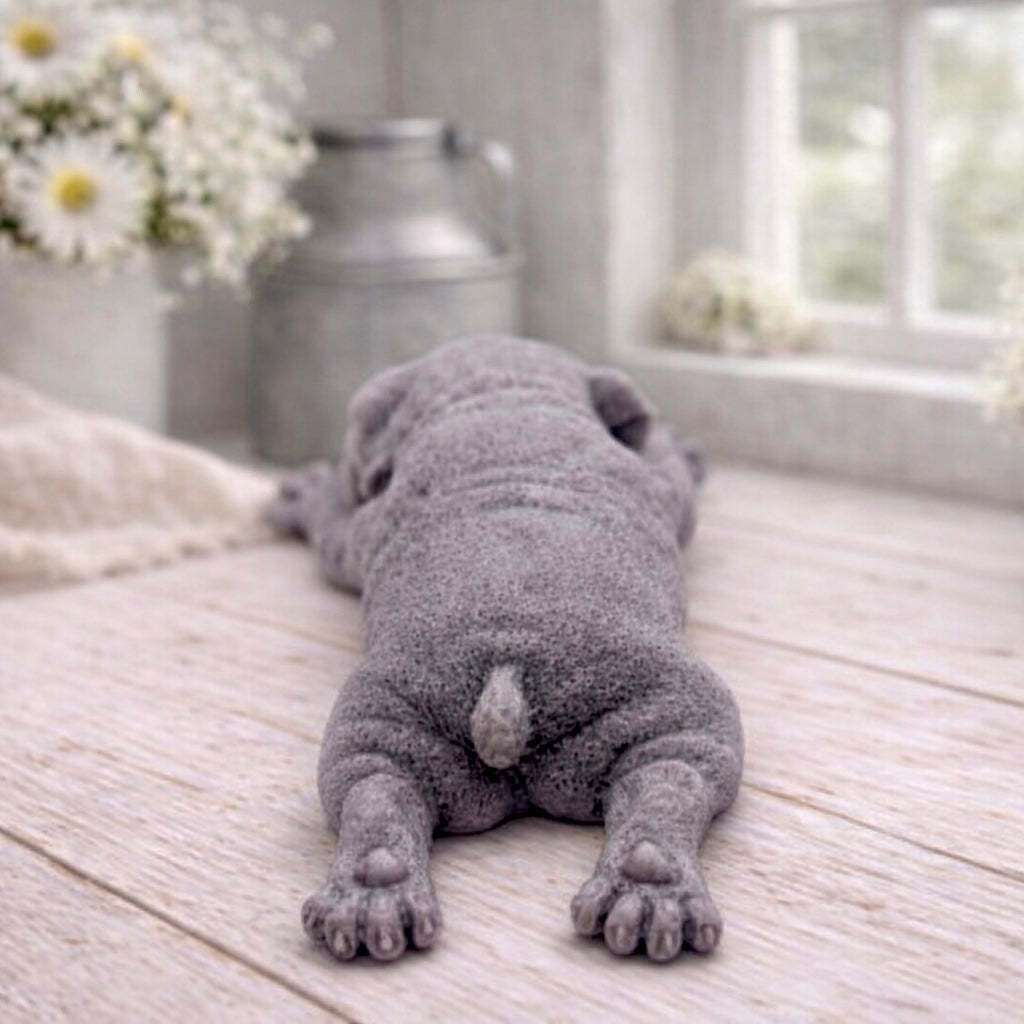 A highly detailed handmade vegan soap in a sophisticated slate-grey tone, sculpted in the shape of a Shar Pei puppy lying flat on its stomach with its head resting on its paws, featuring realistic deep skin folds and wrinkles.