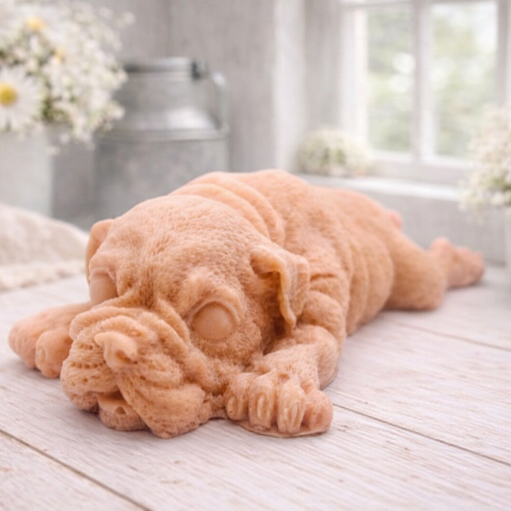 A highly detailed handmade vegan soap in a sophisticated slate-grey tone, sculpted in the shape of a Shar Pei puppy lying flat on its stomach with its head resting on its paws, featuring realistic deep skin folds and wrinkles.