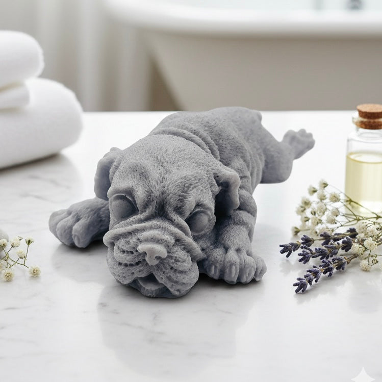 A highly detailed handmade vegan soap in a sophisticated slate-grey tone, sculpted in the shape of a Shar Pei puppy lying flat on its stomach with its head resting on its paws, featuring realistic deep skin folds and wrinkles.
