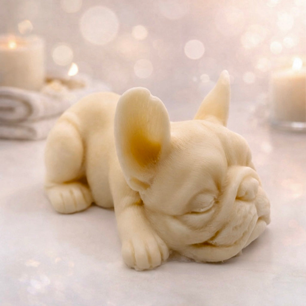 Handmade vegan soap in the shape of a realistic sleeping French Bulldog lying down, showing detailed ear texture and facial wrinkles, surrounded by bubbles in a marble bathroom setting.