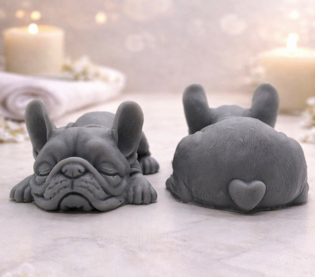 Handmade vegan soap in the shape of a realistic sleeping French Bulldog lying down, showing detailed ear texture and facial wrinkles, surrounded by bubbles in a marble bathroom setting.
