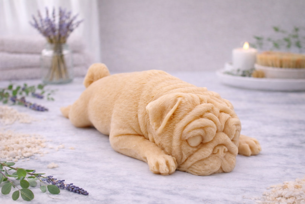 handmade vegan soap in the shape of a realistic sleeping pug dog lying flat, showing detailed wrinkles and fur texture, displayed in a spa-like setting with a candle and lavender.