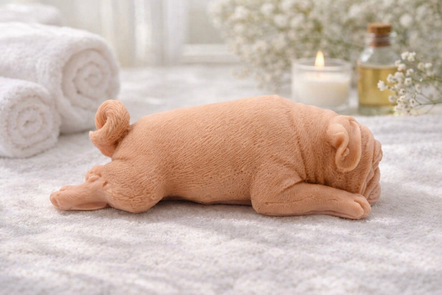 handmade vegan soap in the shape of a realistic sleeping pug dog lying flat, showing detailed wrinkles and fur texture, displayed in a spa-like setting with a candle and lavender.