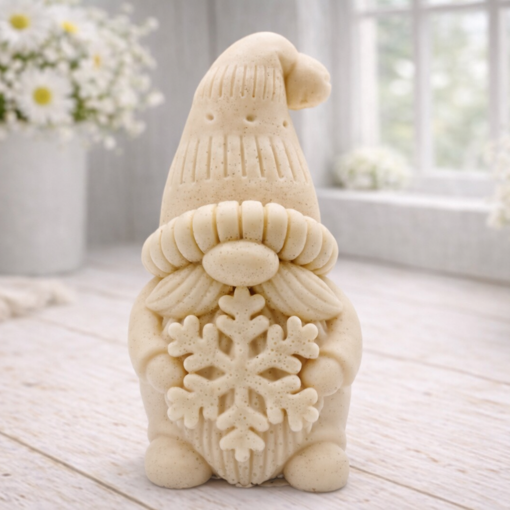 handmade vegan soap in the shape of a winter gnome sculpture holding a large snowflake, featuring a tall textured hat and a bushy moustache , displayed on a rustic white wooden surface with daisies and a milk churn in the background.