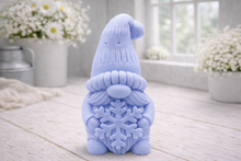 Load image into Gallery viewer, handmade vegan soap in the shape of a winter gnome sculpture holding a large snowflake, featuring a tall textured hat and a bushy mustache, displayed on a rustic white wooden surface with daisies and a milk churn in the background.
