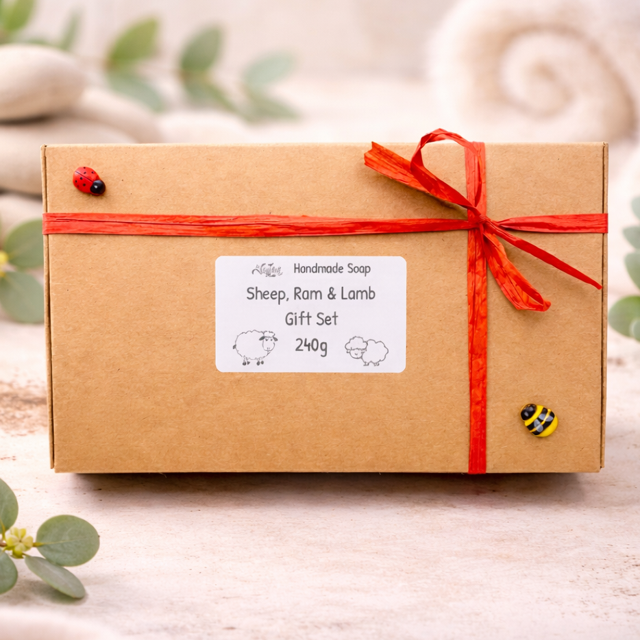 A set of three handmade vegan soaps in different sheep styles, including a dark grey smiling sheep and two lambs with detailed woolly textures, displayed on a rustic wooden surface with lavender and flowers.