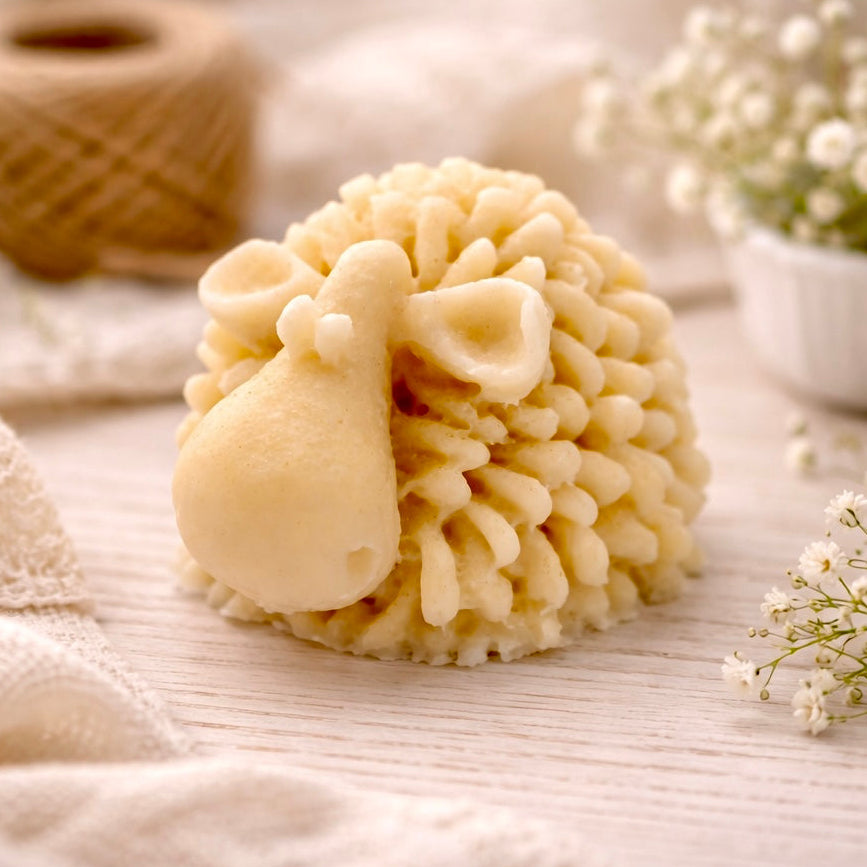 A set of three handmade vegan soaps in different sheep styles, including a dark grey smiling sheep and two lambs with detailed woolly textures, displayed on a rustic wooden surface with lavender and flowers.