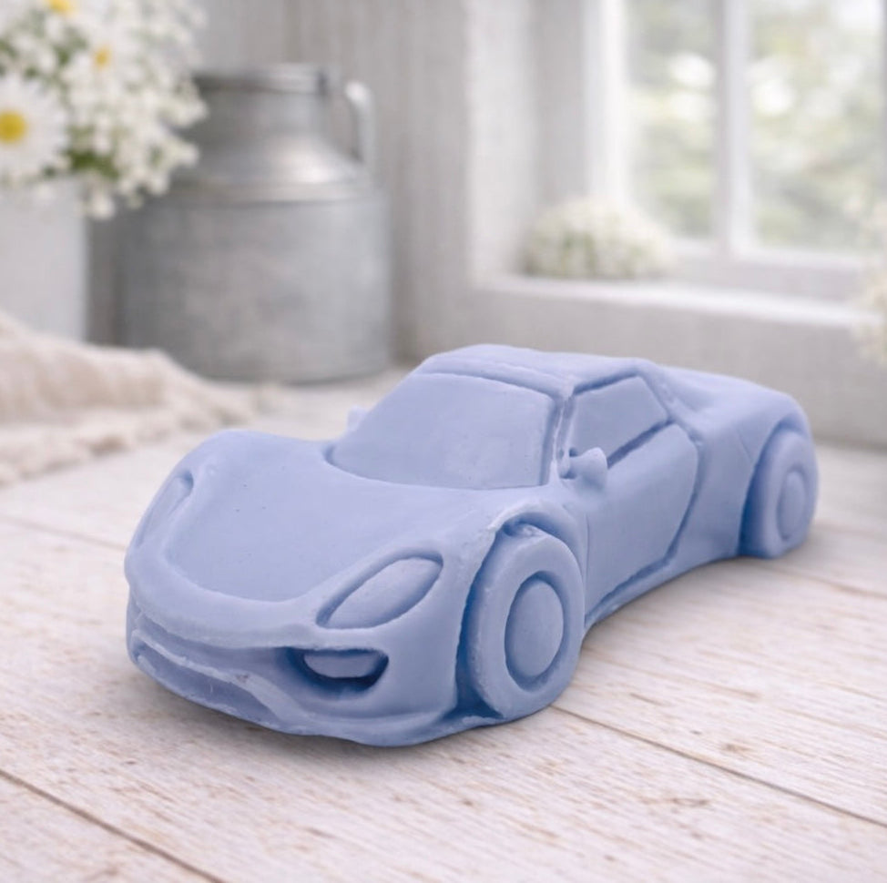 handmade vegan soap in the shape of a sleek supercar sculpture, featuring aerodynamic curves and detailed wheels, displayed on a rustic white wooden surface in a bright farmhouse decor setting.