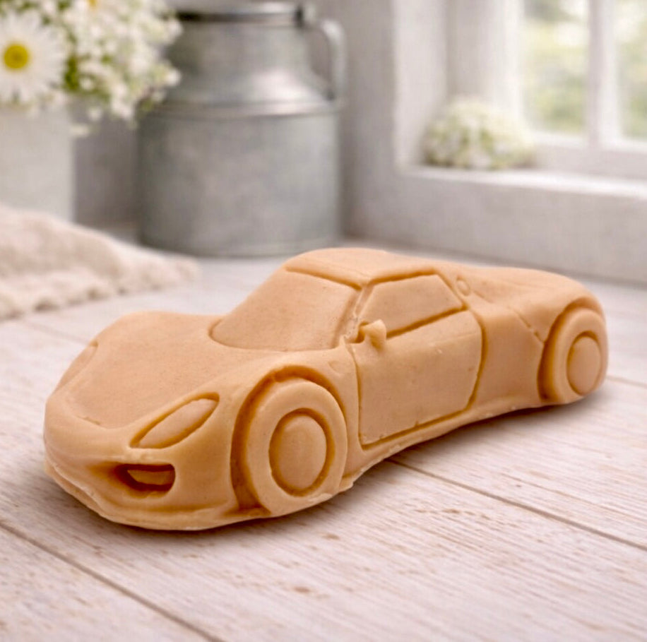 handmade vegan soap in the shape of a sleek supercar sculpture, featuring aerodynamic curves and detailed wheels, displayed on a rustic white wooden surface in a bright farmhouse decor setting.