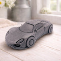 handmade vegan soap in the shape of a sleek supercar sculpture, featuring aerodynamic curves and detailed wheels, displayed on a rustic white wooden surface in a bright farmhouse decor setting.