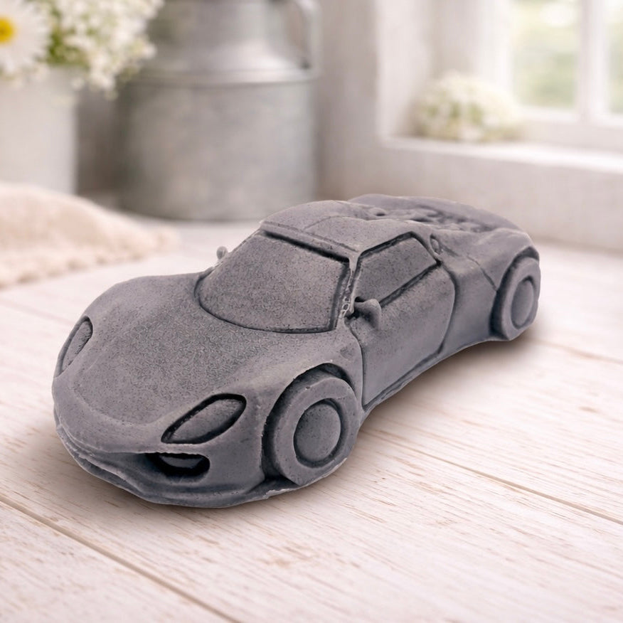 handmade vegan soap in the shape of a sleek supercar sculpture, featuring aerodynamic curves and detailed wheels, displayed on a rustic white wooden surface in a bright farmhouse decor setting.
