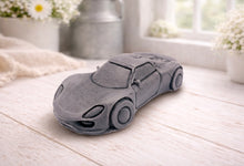 Load image into Gallery viewer, handmade vegan soap in the shape of a sleek supercar sculpture, featuring aerodynamic curves and detailed wheels, displayed on a rustic white wooden surface in a bright farmhouse decor setting.
