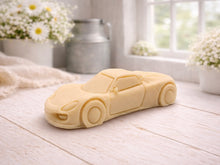 Load image into Gallery viewer, handmade vegan soap in the shape of a sleek supercar sculpture, featuring aerodynamic curves and detailed wheels, displayed on a rustic white wooden surface in a bright farmhouse decor setting.
