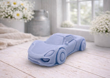 Load image into Gallery viewer, handmade vegan soap in the shape of a sleek supercar sculpture, featuring aerodynamic curves and detailed wheels, displayed on a rustic white wooden surface in a bright farmhouse decor setting.
