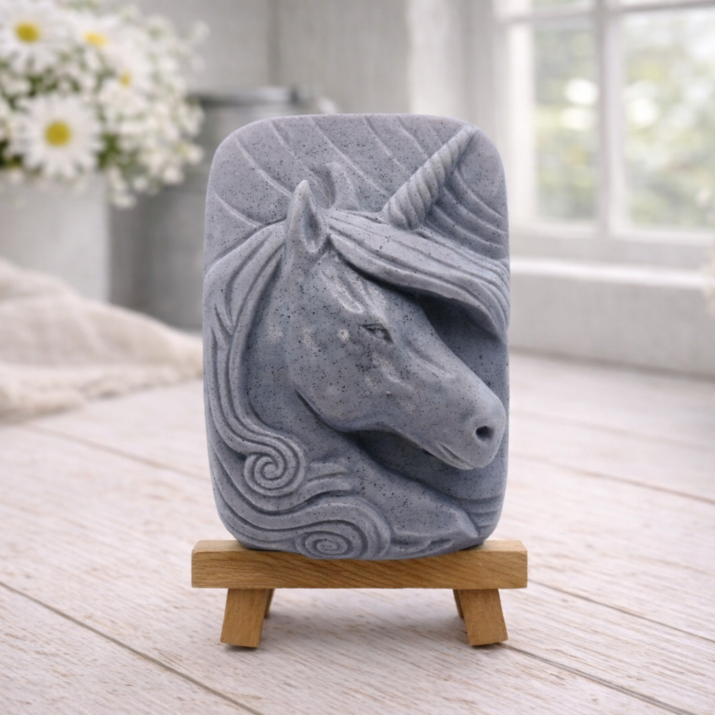 handmade vegan soap featuring a detailed unicorn head relief with a spiralled horn and flowing curly mane, displayed on a small wooden easel in a bright farmhouse decor setting.