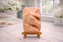 Load image into Gallery viewer, handmade vegan soap featuring a detailed unicorn head relief with a spiralled horn and flowing curly mane, displayed on a small wooden easel in a bright farmhouse decor setting.
