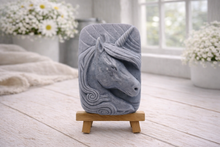 Load image into Gallery viewer, handmade vegan soap featuring a detailed unicorn head relief with a spiralled horn and flowing curly mane, displayed on a small wooden easel in a bright farmhouse decor setting.
