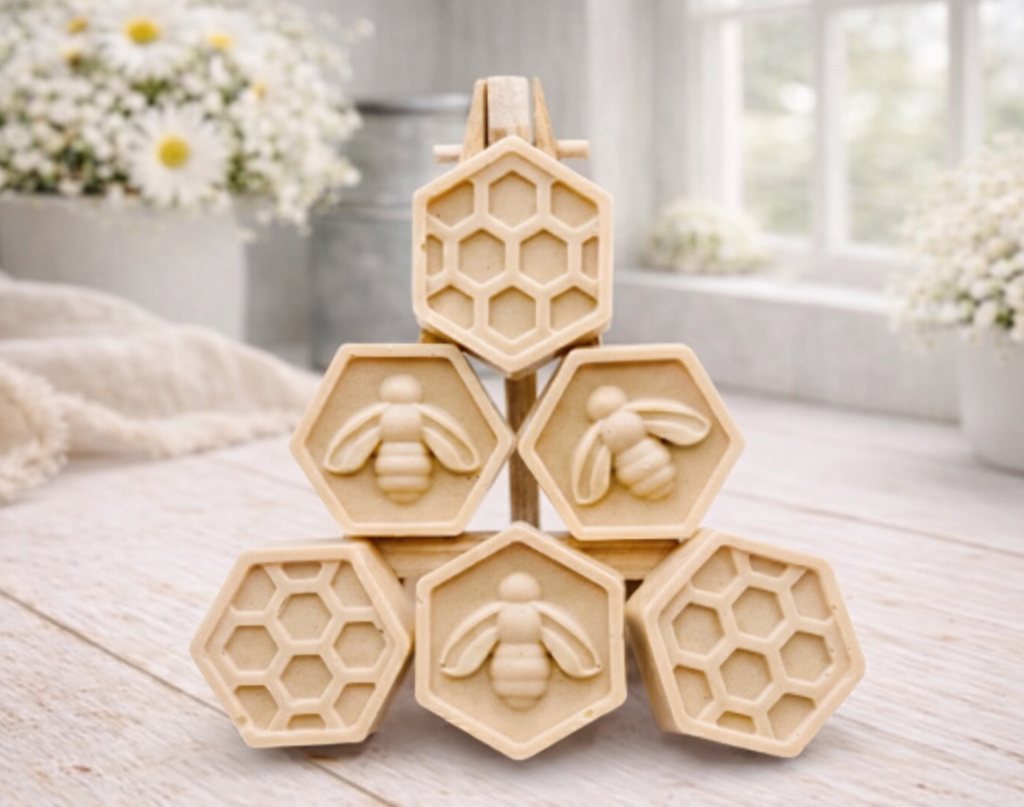 A handmade vegan soap gift set featuring six hexagonal bars stacked in a pyramid on a small wooden easel; some bars show a honeybee relief and others a honeycomb pattern