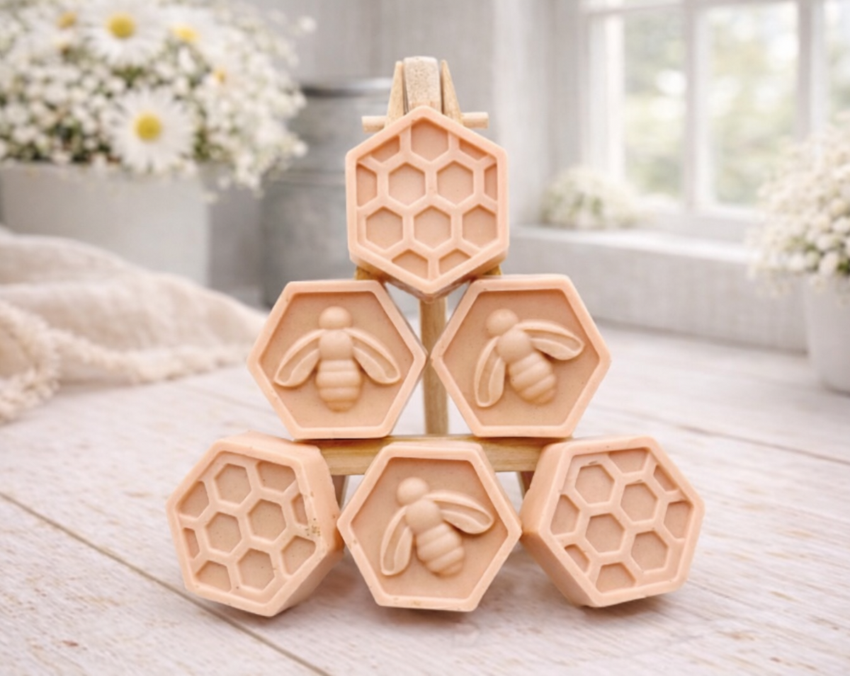 A handmade vegan soap gift set featuring six hexagonal bars stacked in a pyramid on a small wooden easel; some bars show a honeybee relief and others a honeycomb pattern