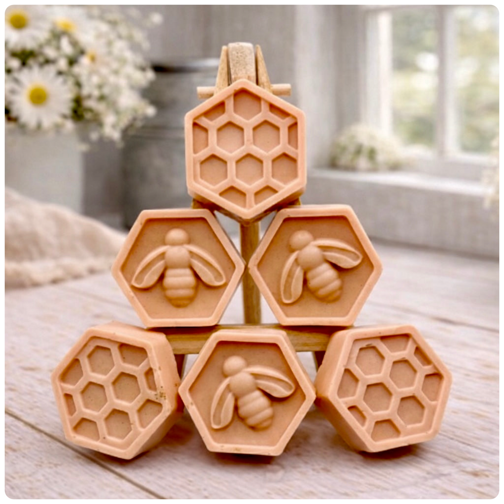 A handmade vegan soap gift set featuring six hexagonal bars stacked in a pyramid on a small wooden easel; some bars show a honeybee relief and others a honeycomb pattern